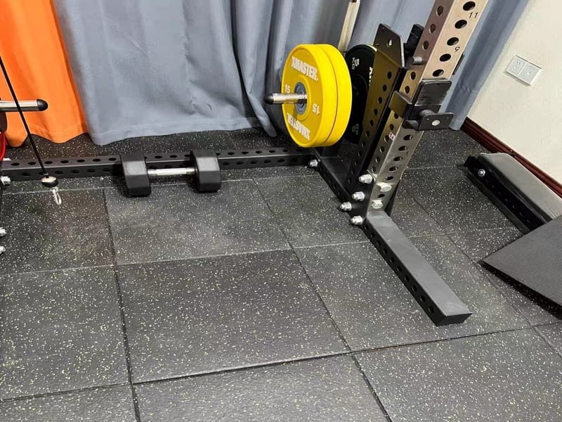 A bottle of pH-neutral cleaner next to a mop on a clean rubber gym floor.